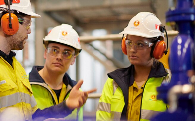 Three workers communicating on site - they are wearing hi-vis, hard hates, ear and eye protection